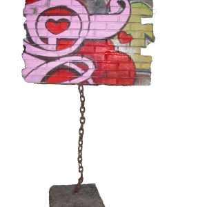 A modern art sculpture consisting in a square piece of a brick wall painted with graffiti floating off the ground trying to fly away but a strong heavy chain keep it connected to the ground. Artwork by Dado