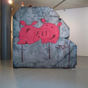 A big rock sculpture with two wool made flat pig characters stitched in the middle. Artwork by Dado