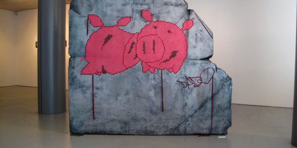 A big rock sculpture with two wool made flat pig characters stitched in the middle. Artwork by Dado