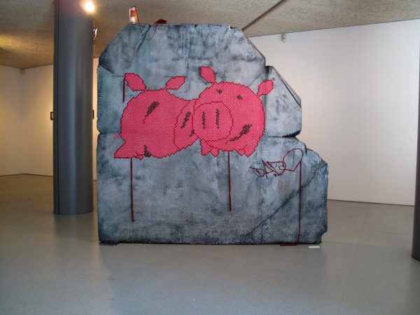 A big rock sculpture with two wool made flat pig characters stitched in the middle. Artwork by Dado