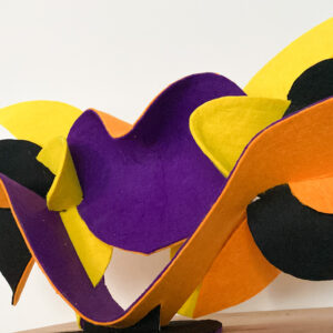 Low front view of a sculpture made of thin bent layers with a soft felt finish in a mix of high saturated yellow, orange, purple and black colors. Artwork by Dado