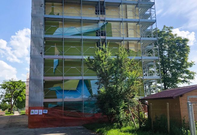 Vista frontale della facciata del palazzo sulla quale è montata l'impalcatura per la realizzazione del dipinto murale Il Valore della Casa dell'artista Dado